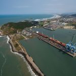 Vista aérea do porto de Imbituba, com navios, cais, guindastes e a faixa litorânea