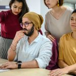 Profissionais colaboram diante de um computador em um escritório moderno.