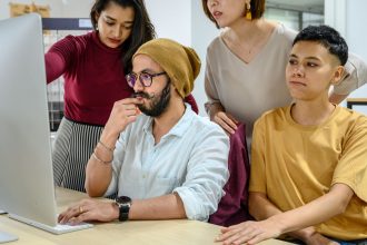 Profissionais colaboram diante de um computador em um escritório moderno.