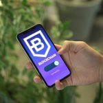 Mão segura um smartphone que exibe a tela de um aplicativo de blockchain.
