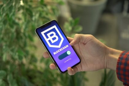 Mão segura um smartphone que exibe a tela de um aplicativo de blockchain.