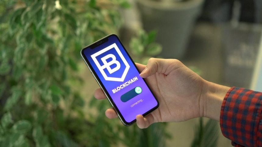 Mão segura um smartphone que exibe a tela de um aplicativo de blockchain.