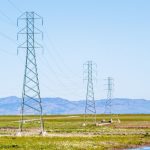 Torres e linhas de transmissão de energia atravessando um amplo campo sob céu claro.