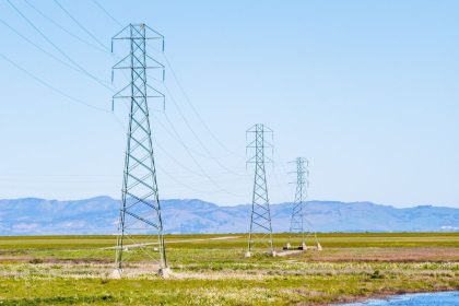 Torres e linhas de transmissão de energia atravessando um amplo campo sob céu claro.