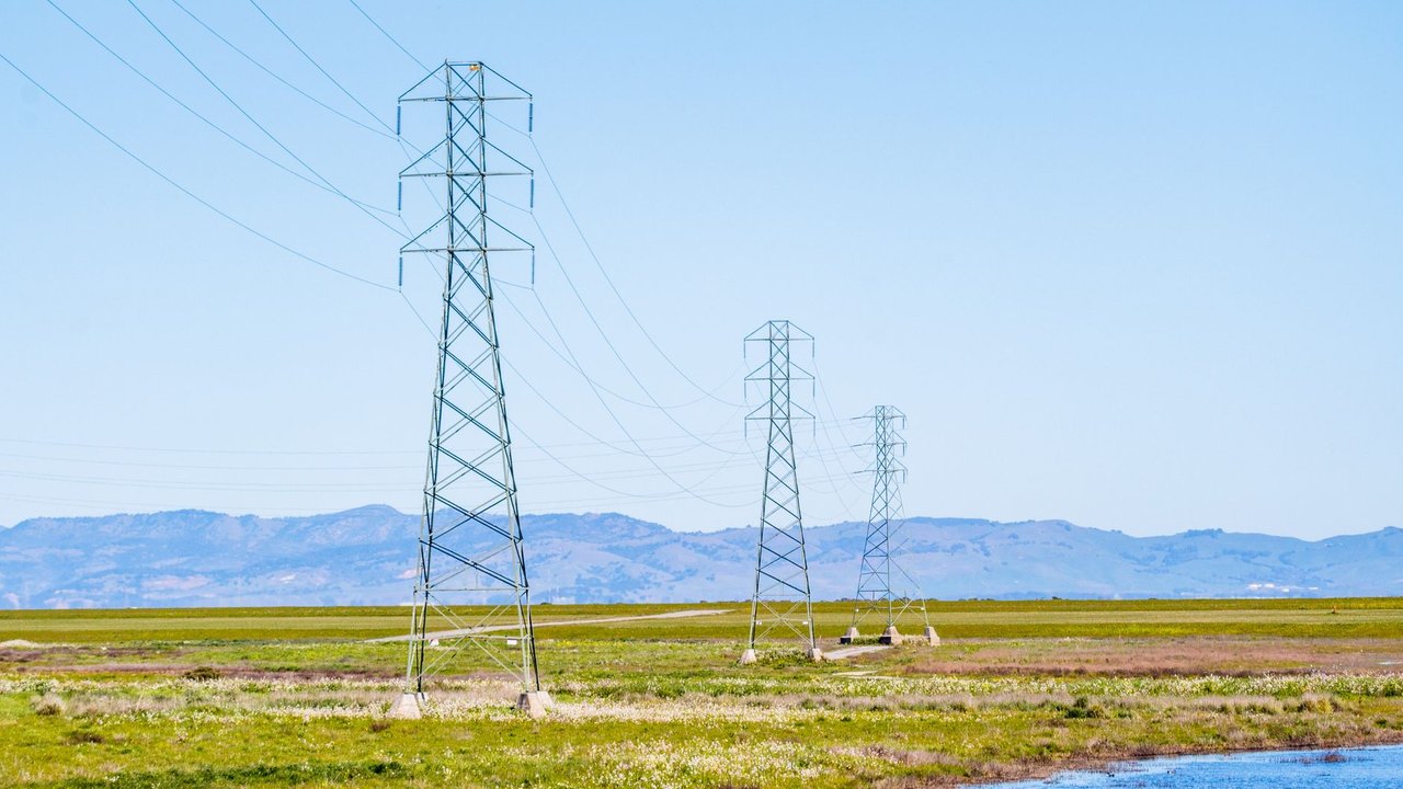 Torres e linhas de transmissão de energia atravessando um amplo campo sob céu claro.
