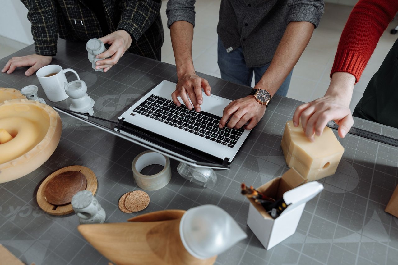 Equipe diversa colaborando em um projeto de inovação tecnológica em uma oficina, com ferramentas e protótipos sobre a mesa.